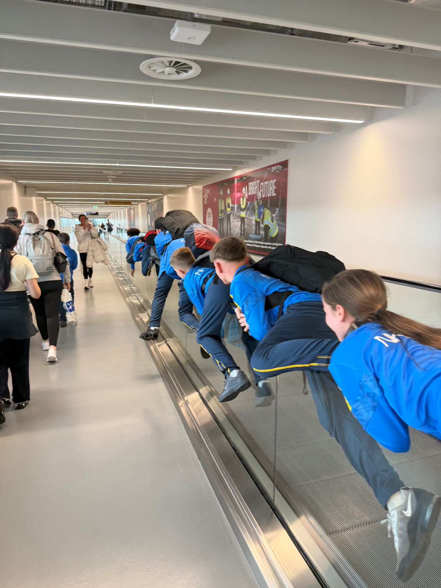 Fletcher Moss Rangers players lean on a travelator in an airport. They ...