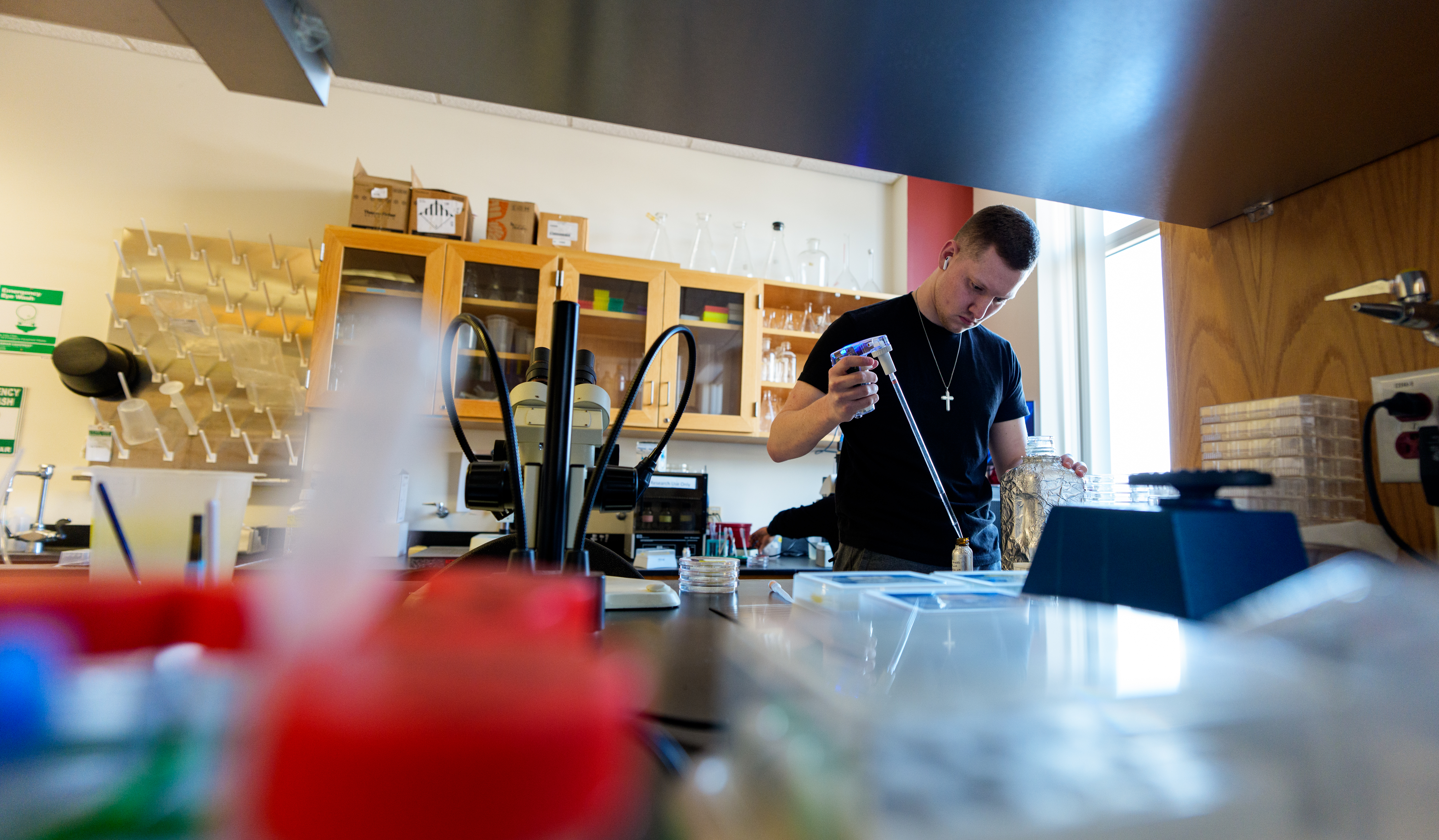 Jacob Starkey works in a zebrafish lab, spraying a clear liquid into a ...