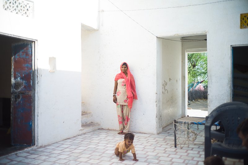 Bhanvari leaning against a wall in her house as her daughter crawls away from her and towards the camera.