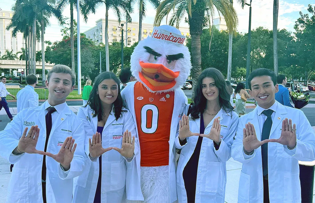 Four smiling medical students in white coats pose with the Miami ...