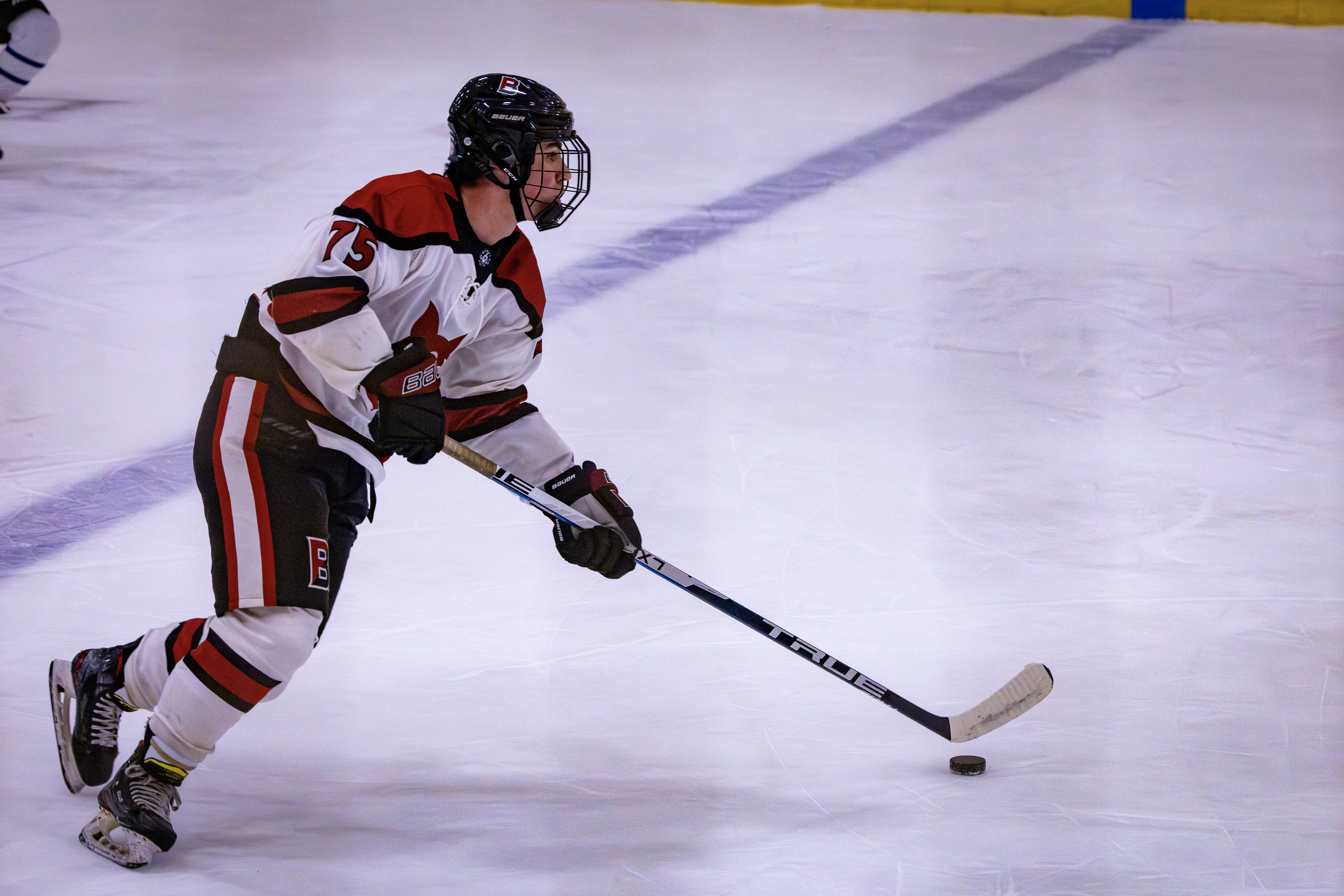 Bates hockey player in white and red uniform skates with stick and puck ...