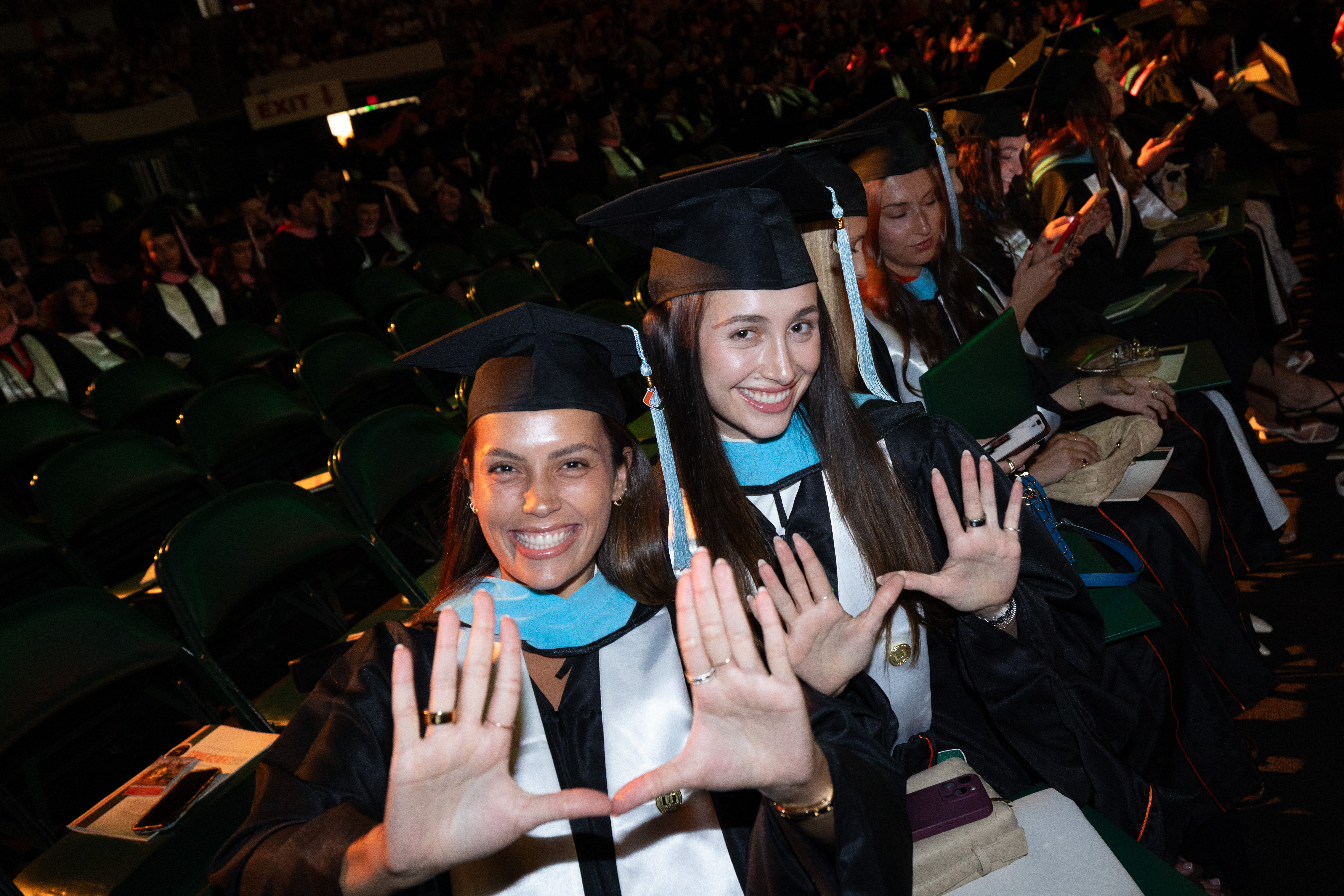 Two smiling graduates in caps and gowns hold up their hands, making a
