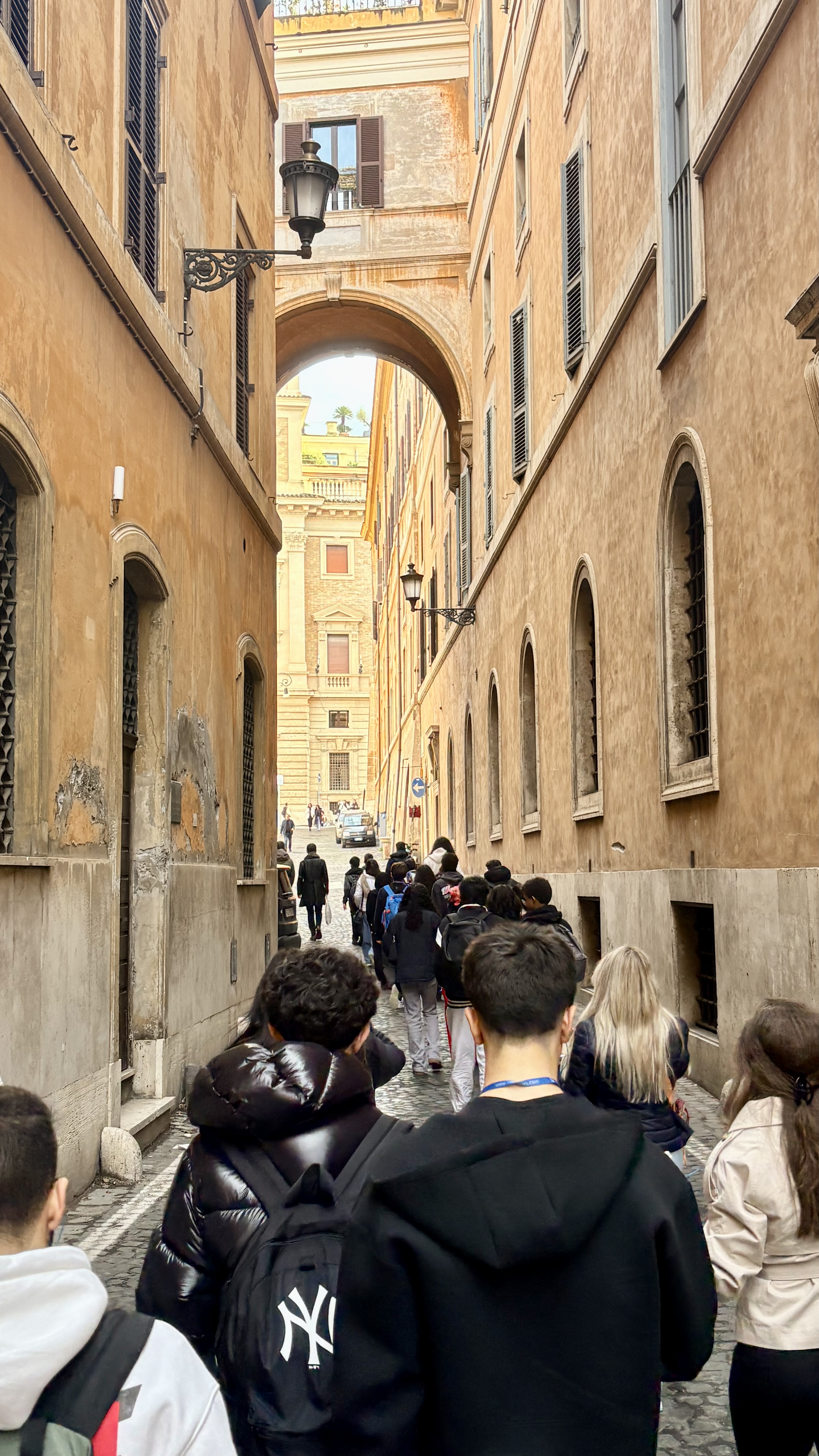 A group walks down a narrow street in Italy. Buildings with arched ...