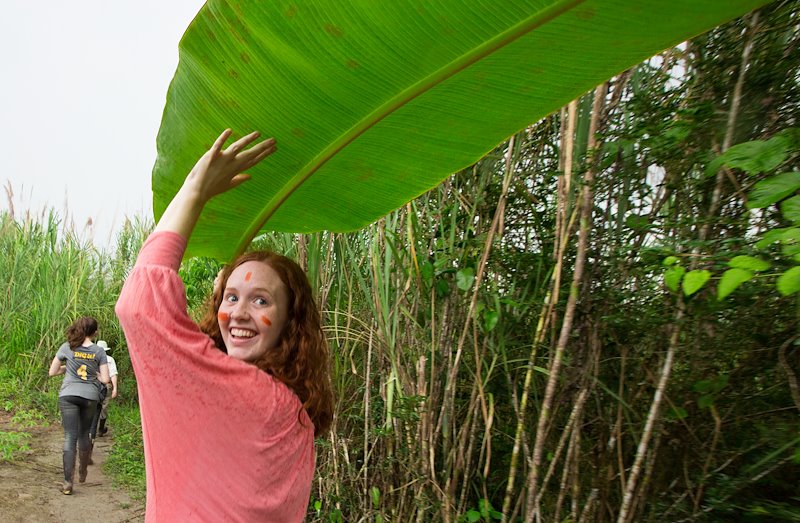 Sydney Jensen uses a banana leaf  as cover during a rainstorm in the jungle.