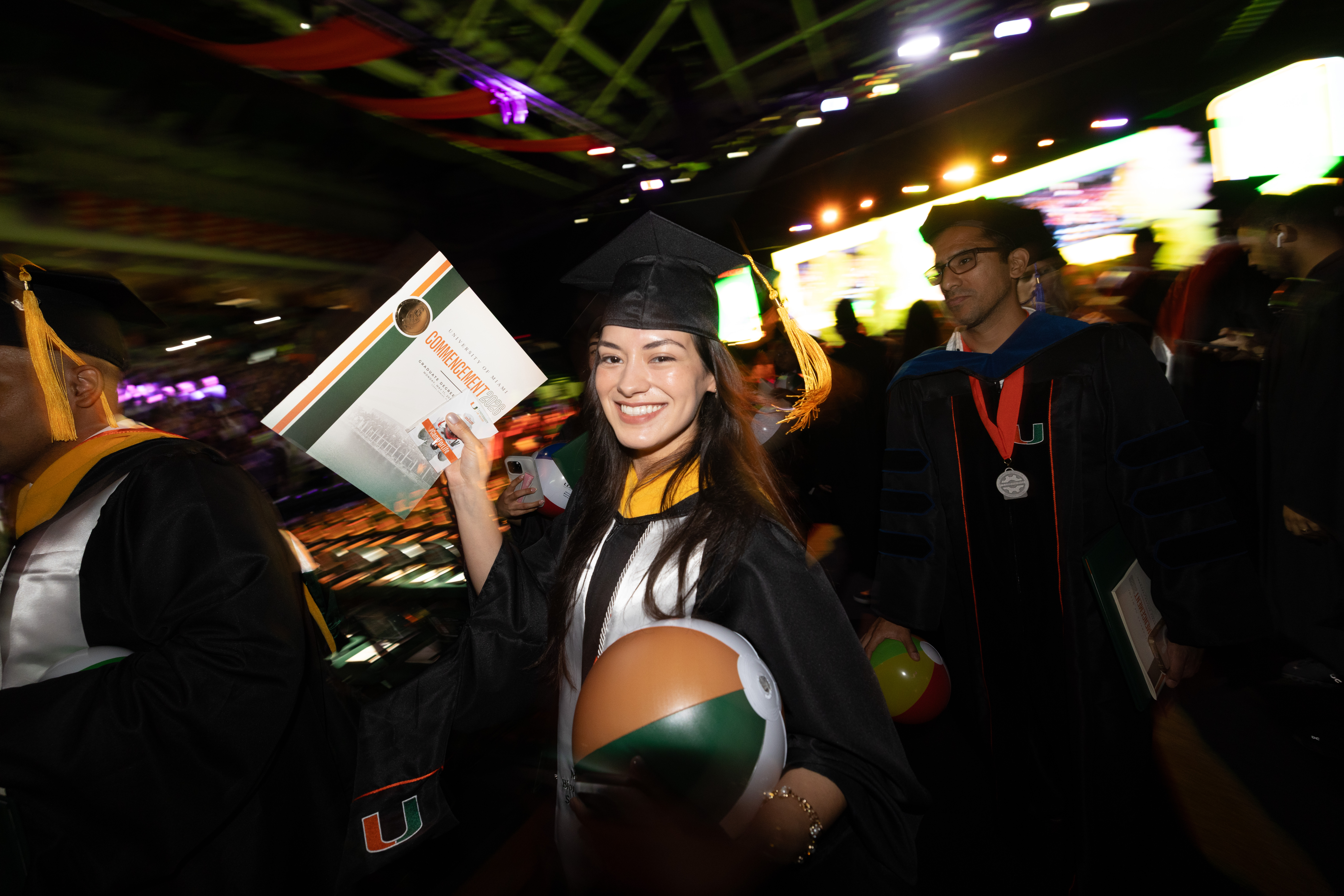Smiling graduate in cap and gown holds diploma and beach ball at the ...