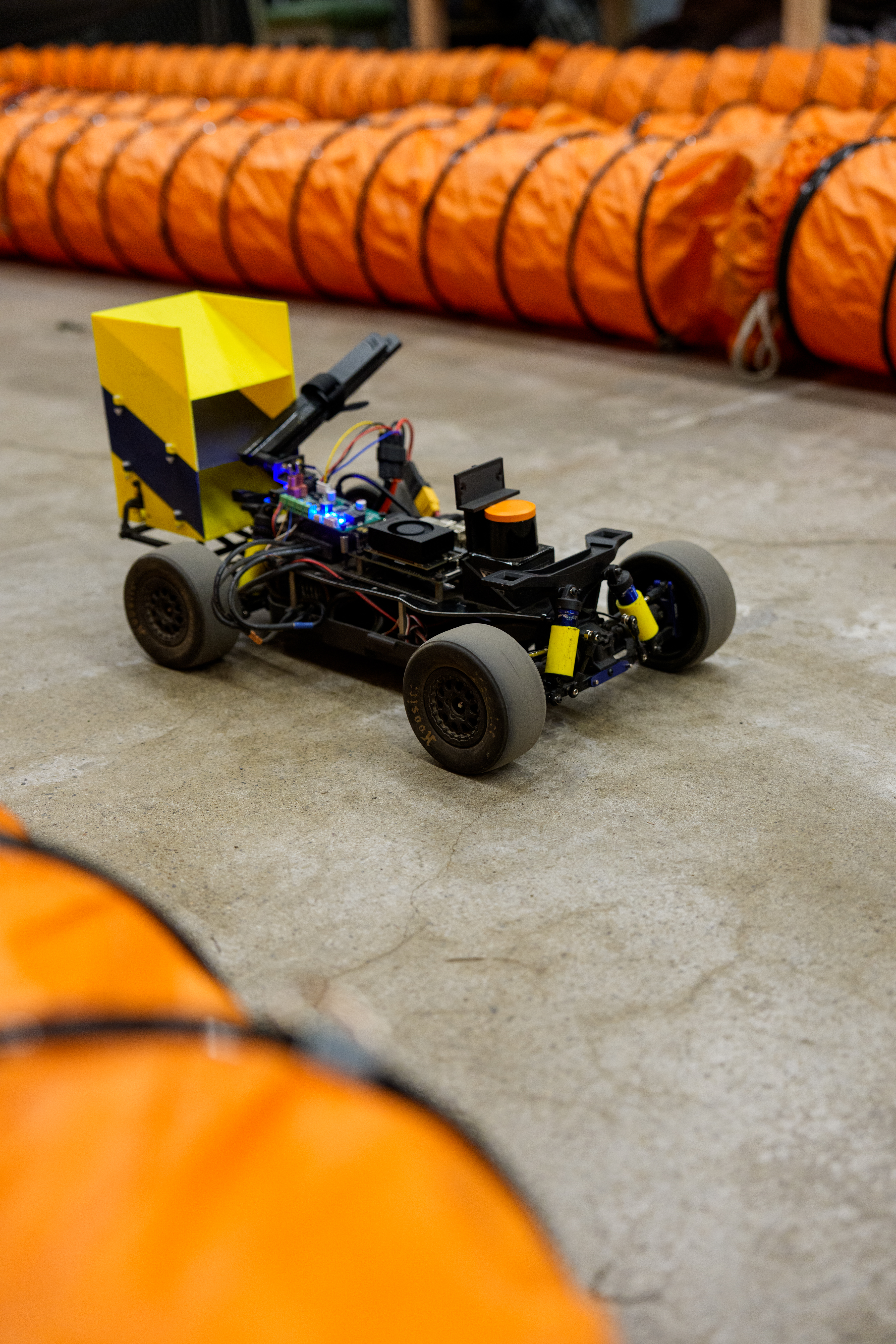 The WVU F1Tenth Roboracer sits on a concrete track in a lab. The ...