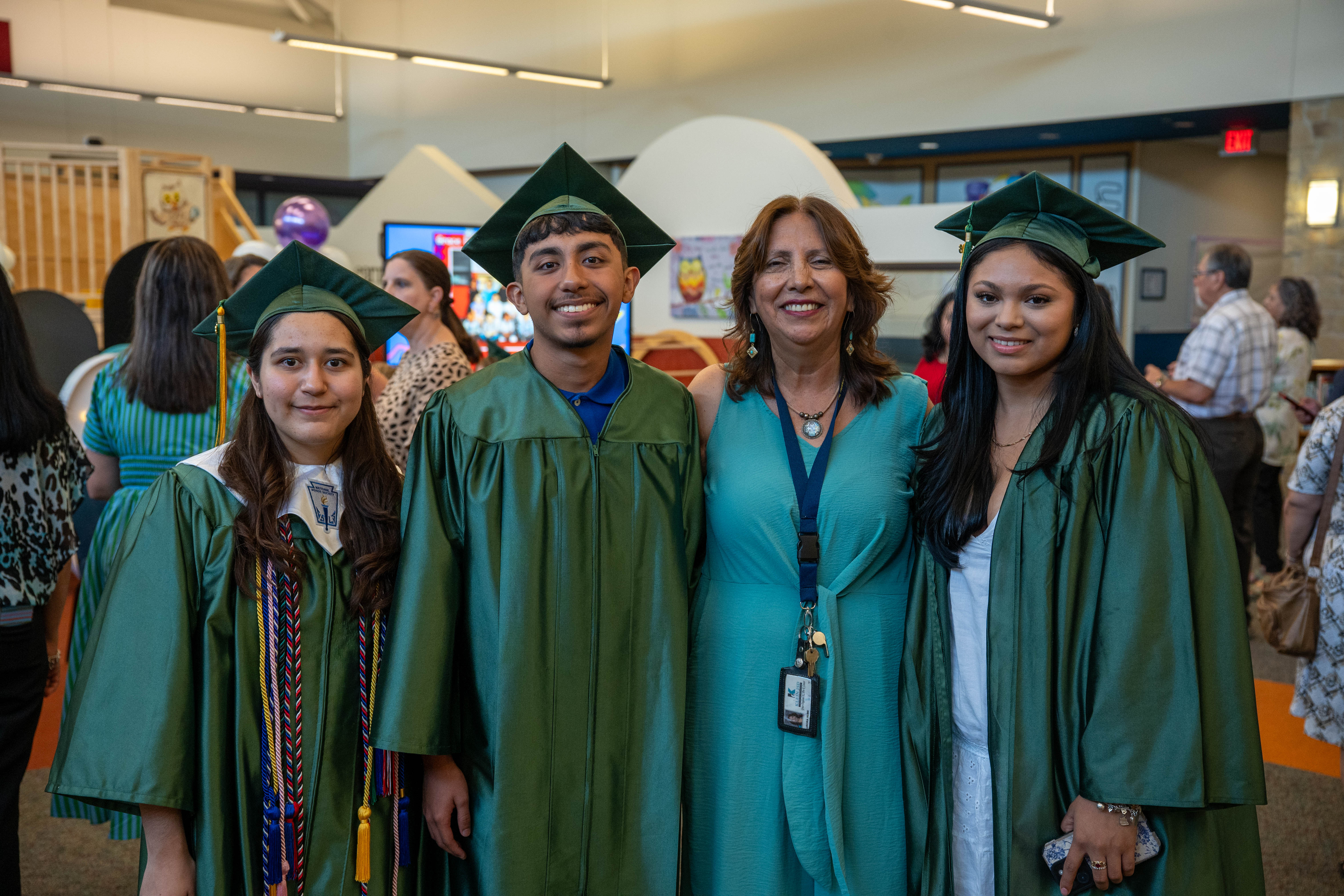 Three graduates in green caps and gowns pose with a woman in a ...