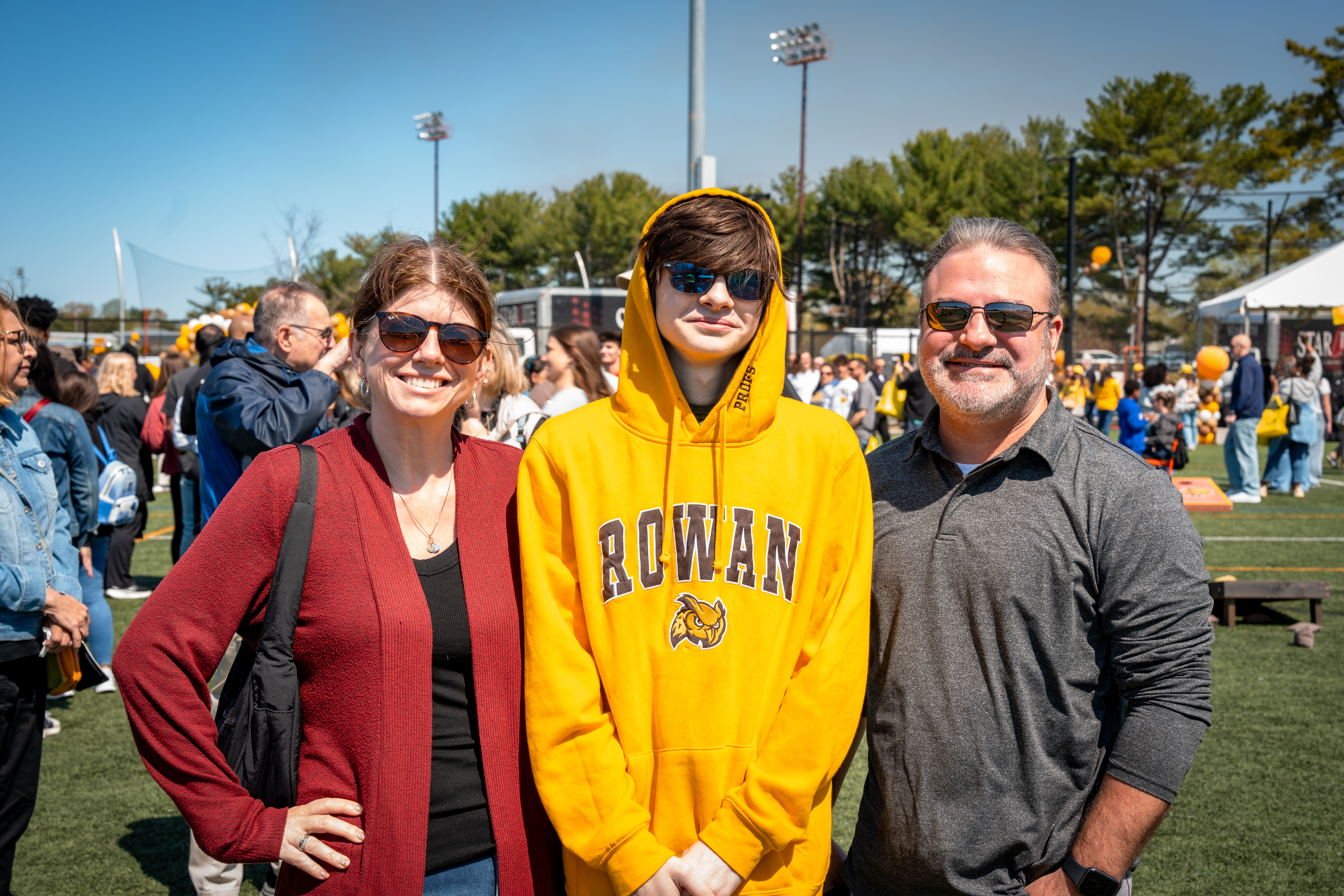 Family stands on a sunny Rowan University campus. The teen wears a gold ...