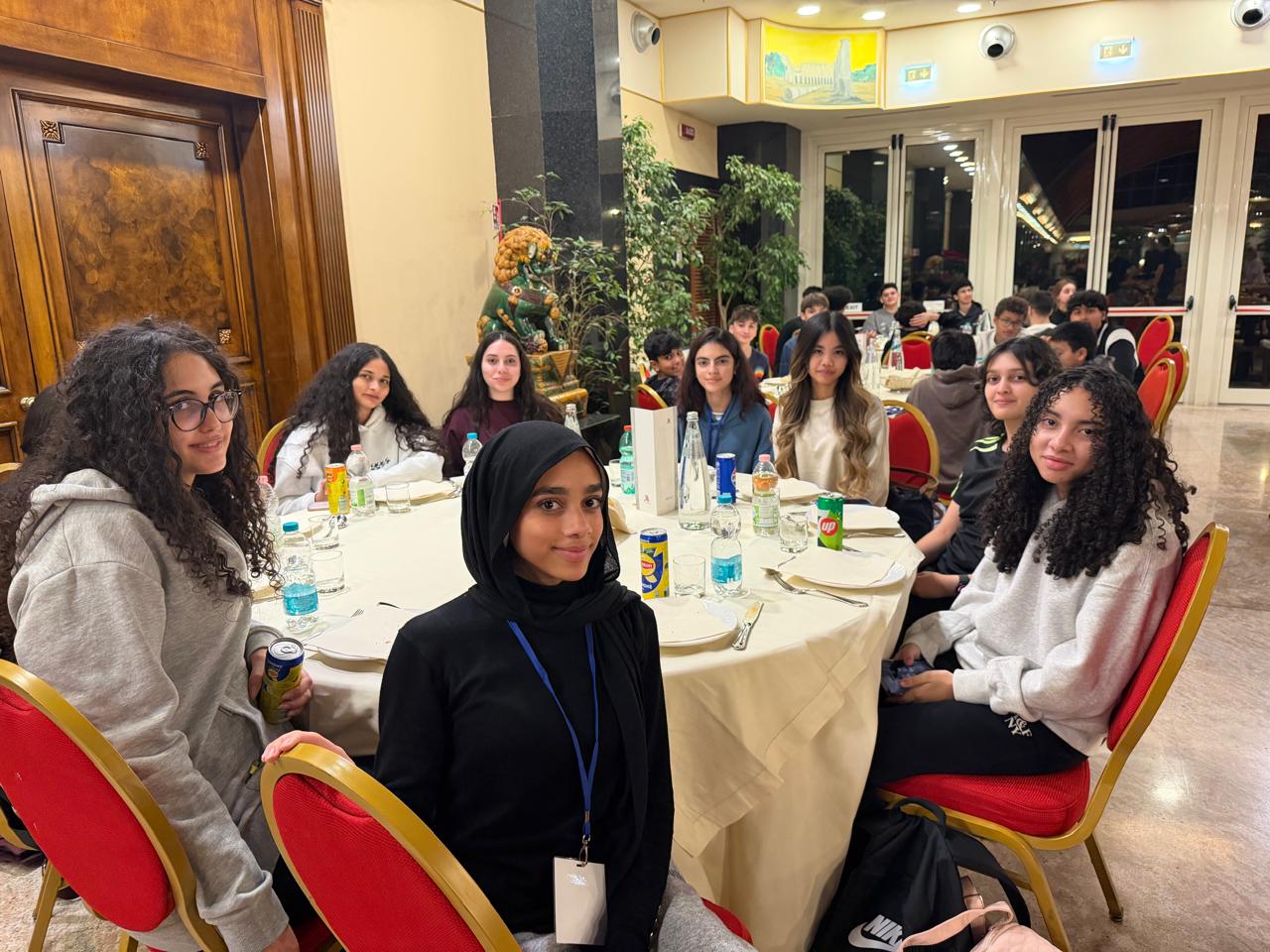 A group of teenage students sit around a round table in a dining room ...
