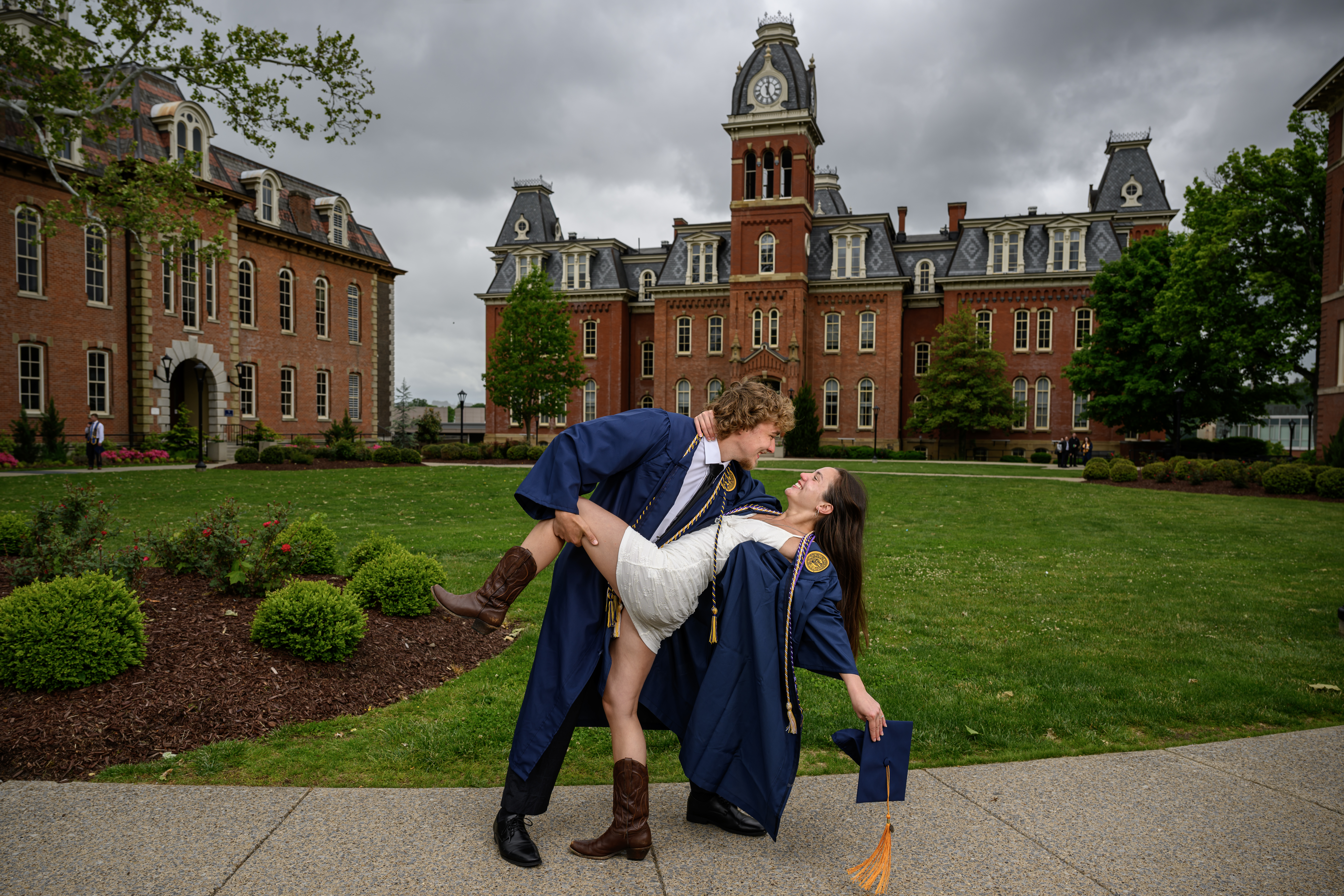 Graduates pose at Woodburn Circle. Man in graduation gown lifts woman ...