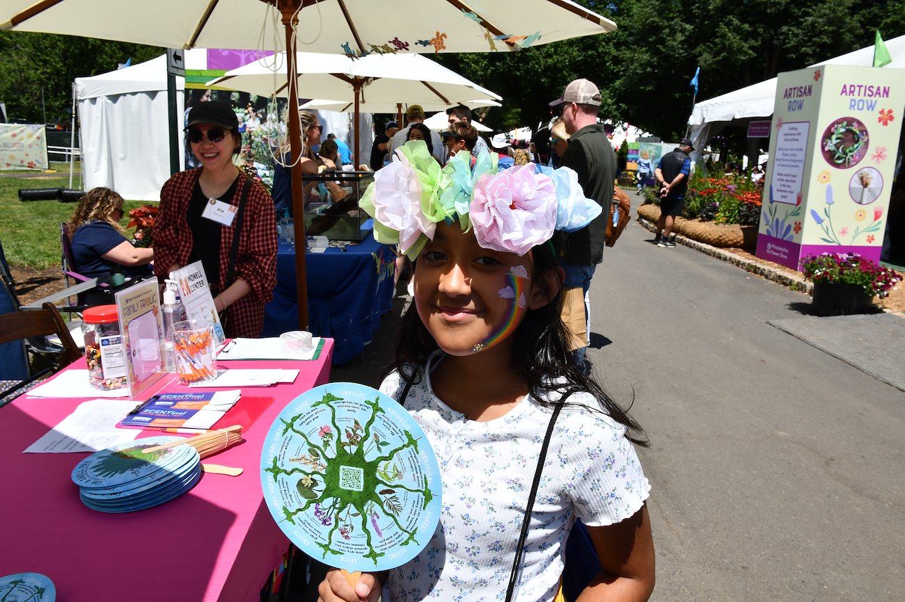 A Flower Show visitor outfitted with the decor of the day and a Smell Fan.
