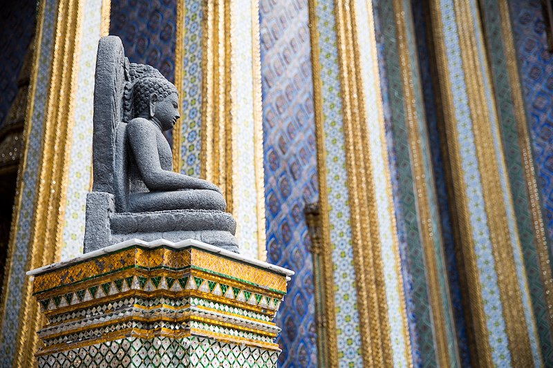 A stone Buddha stands out against the colorful columns of Wat Phra Kaew.