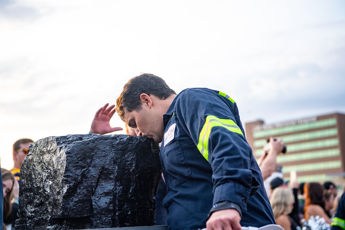 Coal miner in reflective work clothing touches the ceremonial coal during West Virginia University's inaugural 2024 Coal Rush Mountaineer Mantrip