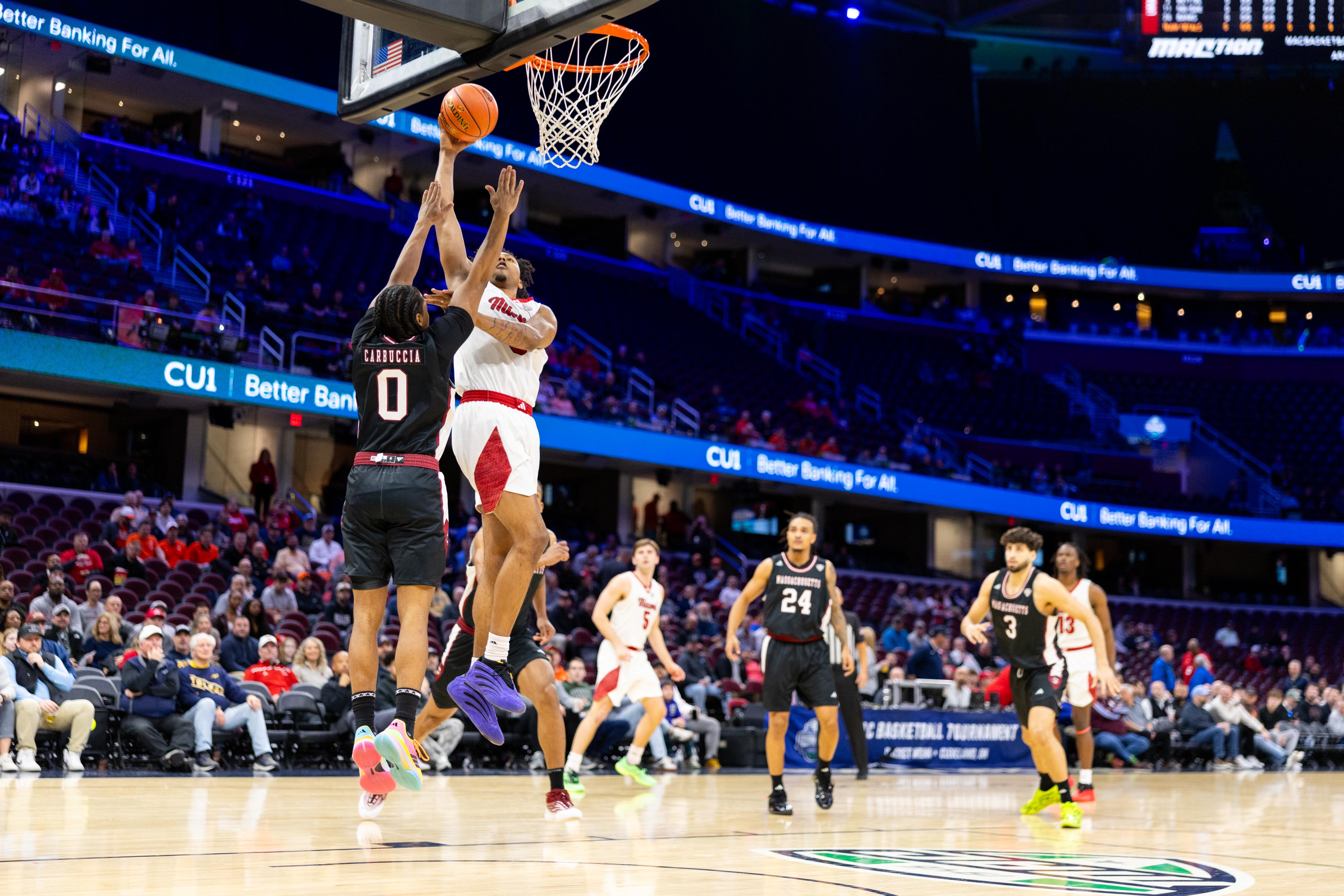A basketball player in white jumps to block a shot by a player in black ...