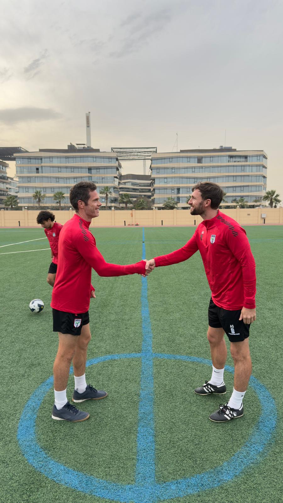 Two soccer players in red jerseys shake hands on a green field with ...