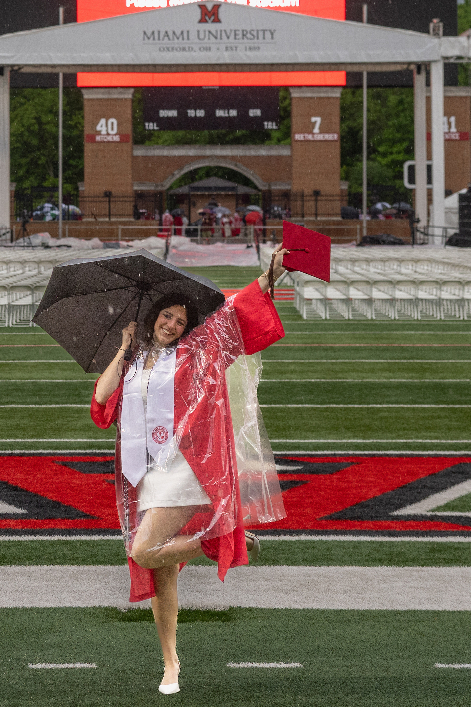 A graduate smiles, holding a cap and umbrella on a rainy day at Miami ...