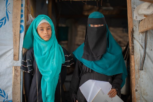 Rania and her eldest daughter, Amani, stand in the entrance to their home in a camp for internally displaced people in Lahj, Yemen. Photo: WFP/Mohammed Awadh