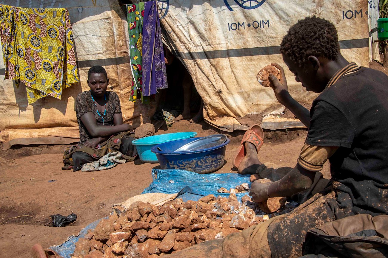 Angele watches her nephew, Dieudonné, smash stones to find bits of gold.