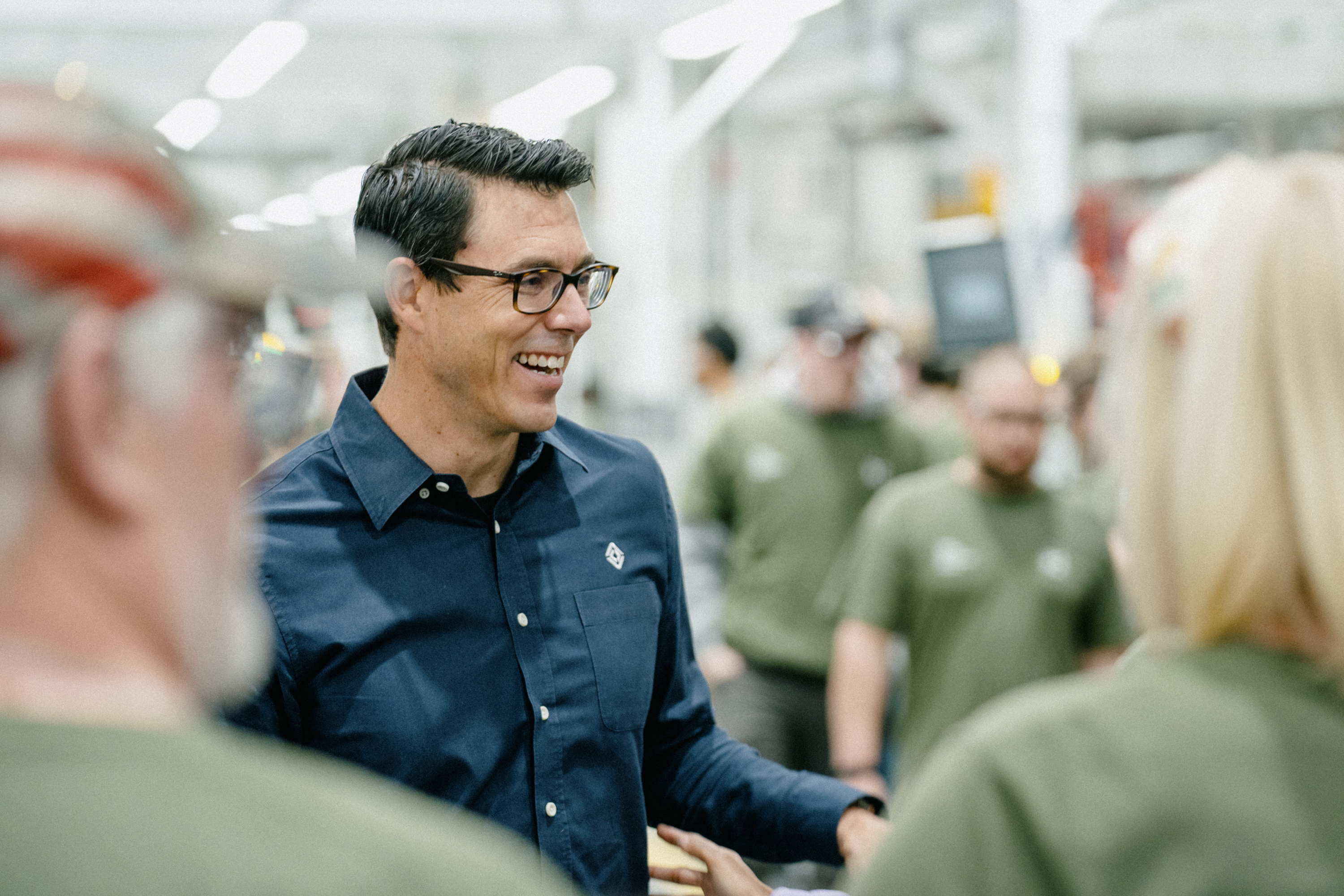A smiling man in glasses and a Rivian shirt stands in a factory ...