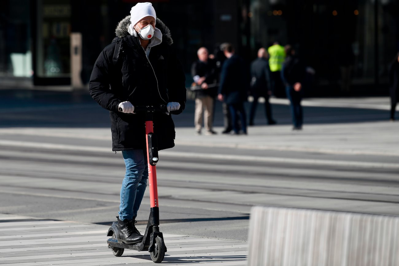 A man, wearing a protective mask and disposable gloves, rides an electric scooter in Stockholm, Sweden, on Thursday, March 26, 2020.