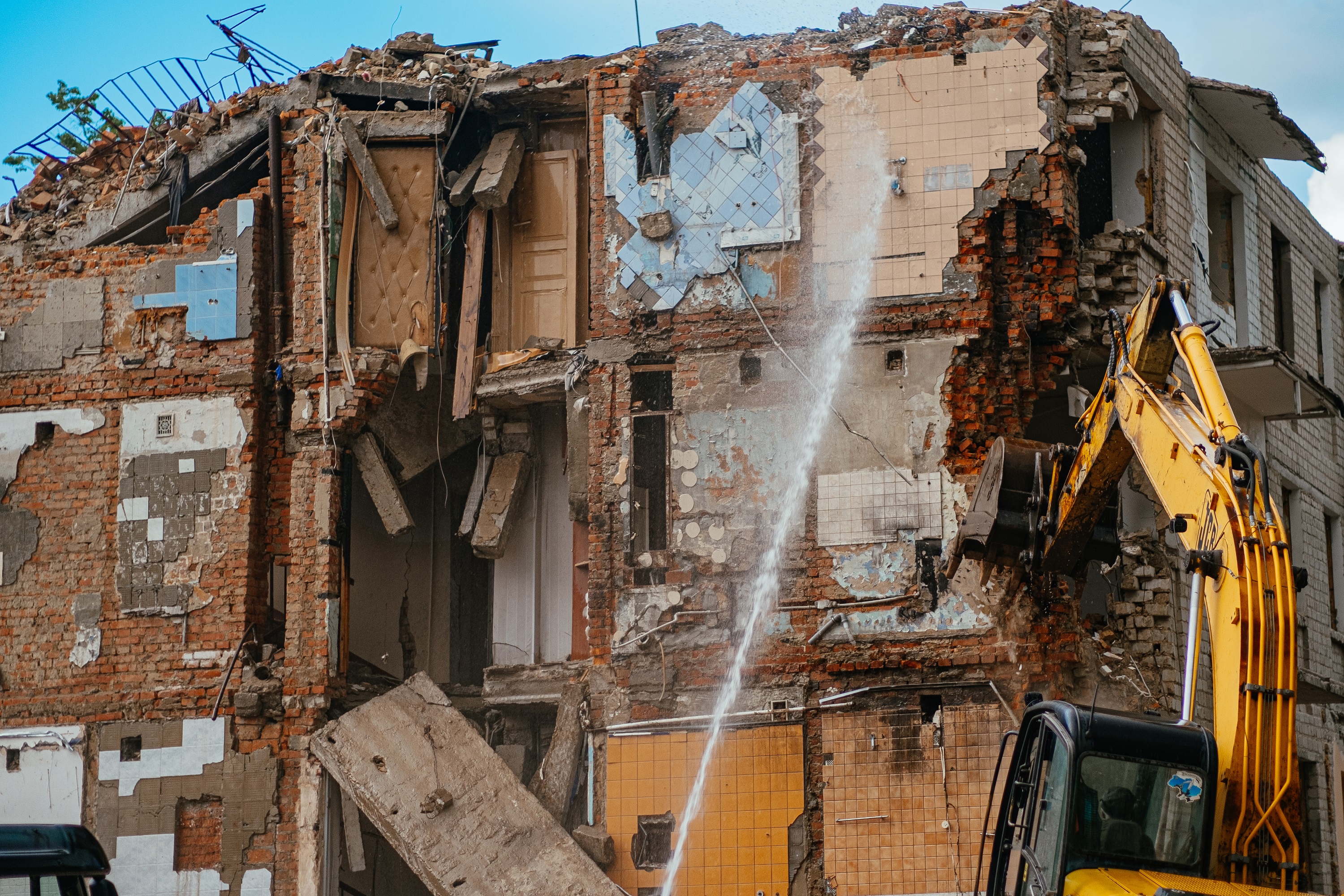 Excavator demolishes damaged building, spraying water. The brick ...