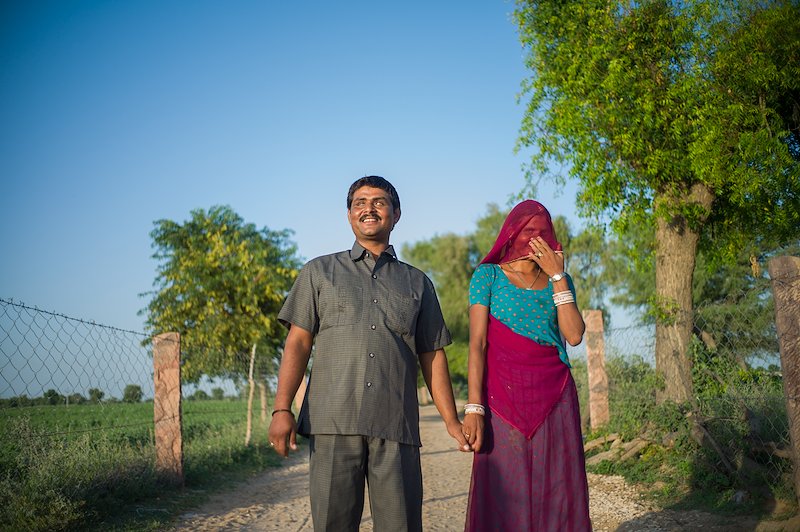 Sankarlal and his wife Gomati walking along a tree-lined track. He is smiling and she is laughing behind her hand.