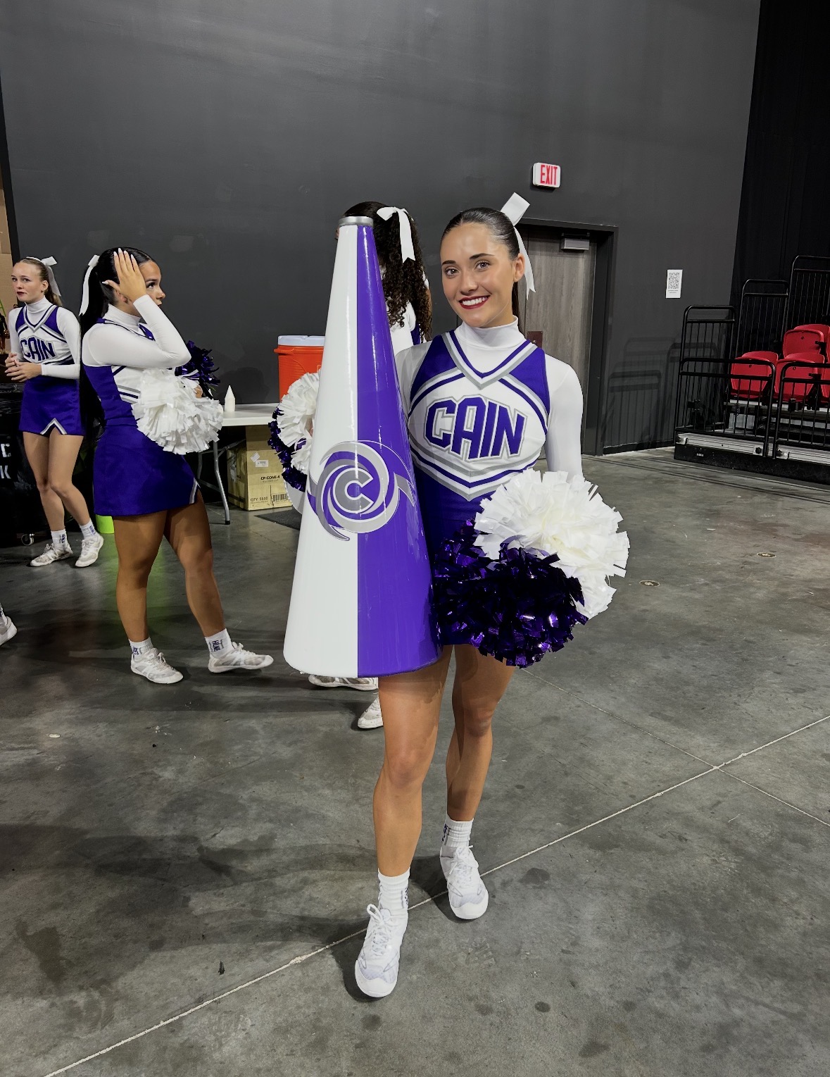 A smiling cheerleader in a purple and white uniform holds a matching ...