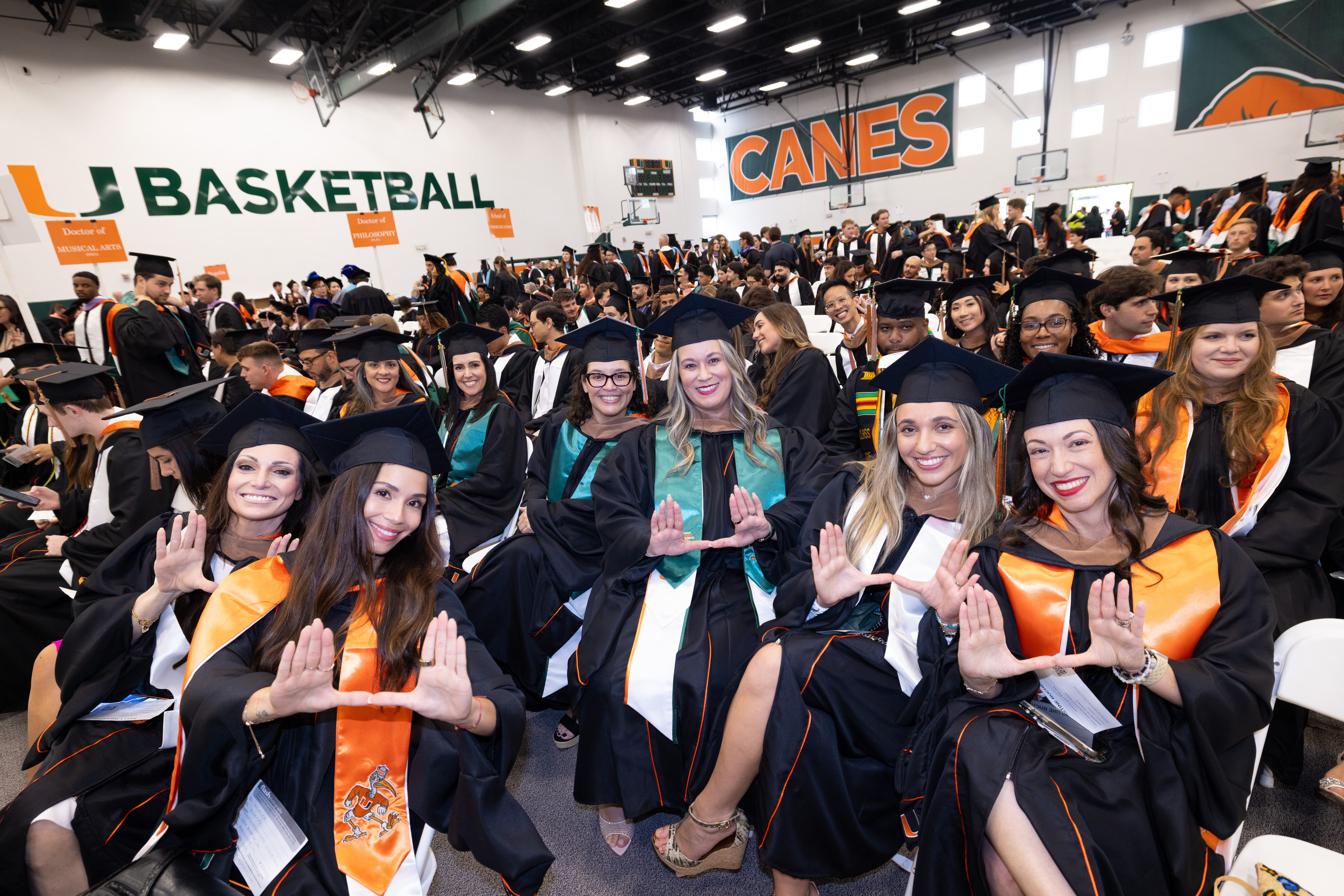 Graduates in black gowns and caps sit in rows at the Spring 2026 ...